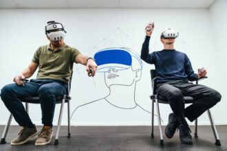 Two men seated on chairs, wearing virtual reality headsets, engaged in an immersive digital experience of pilot training provided by Air Bus and Lufthansa Aviation Training.