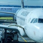Two Air New Zealand aircraft parked at an airport gate, one connected to a jet bridge.