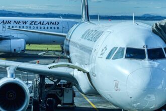 Two Air New Zealand aircraft parked at an airport gate, one connected to a jet bridge.
