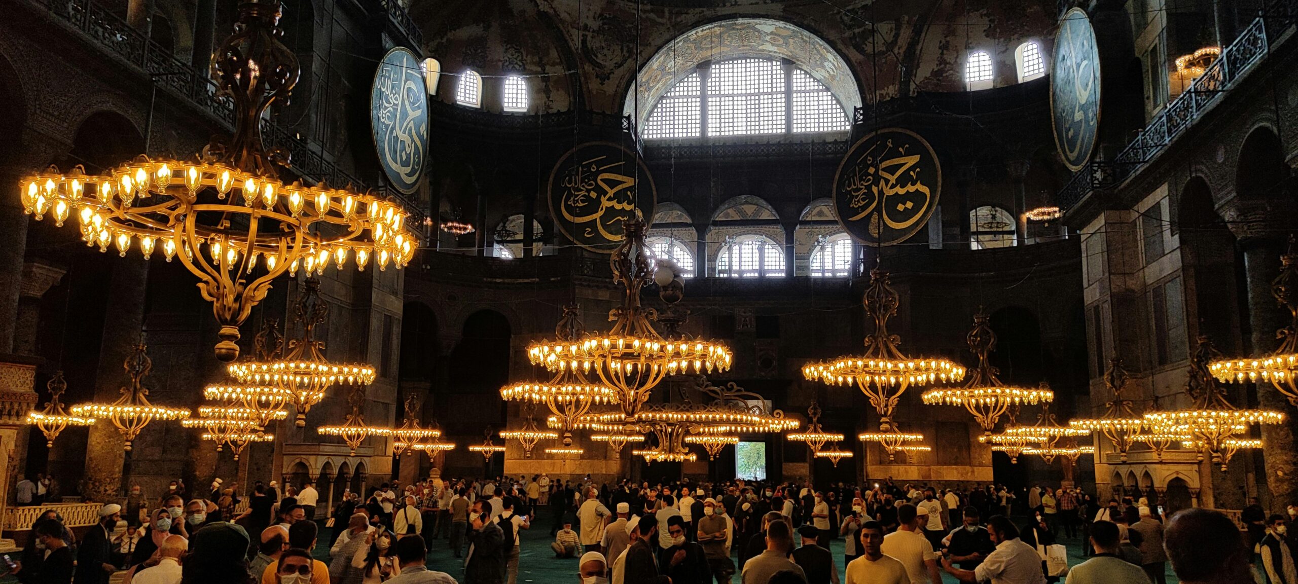 Inside Hagia Sofia Grand Mosque, Istanbul. There are chandeliers with candles illuminating the faces of the people inside.