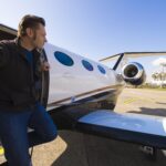 Man stepping out from a private jet under a clear blue sky. Climate