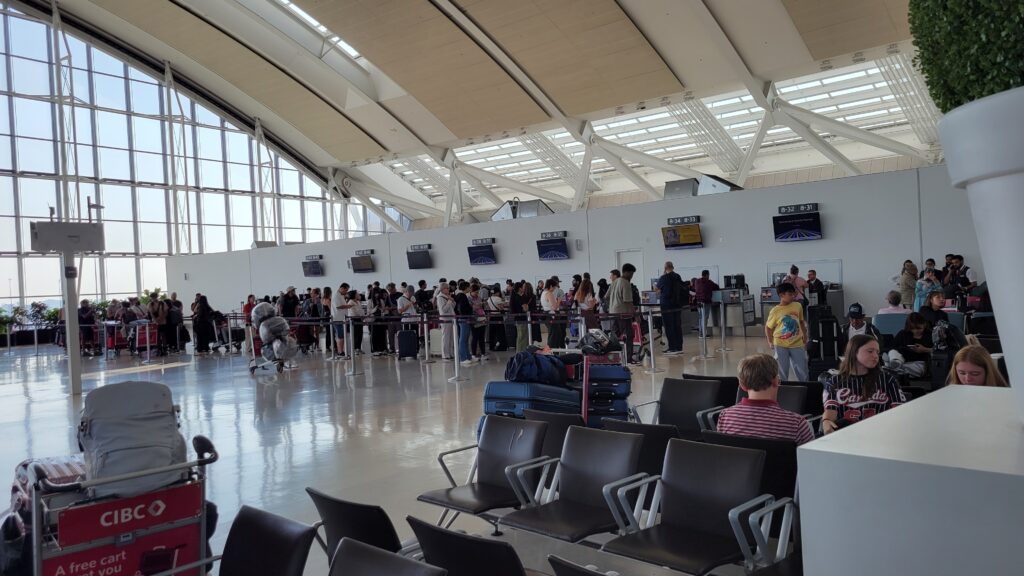 Support desk for US-bound Air Canada passengers that are affected by the flight attendant strike inside a bright, modern airport terminal, with luggage carts and waiting area seats visible in the foreground.
