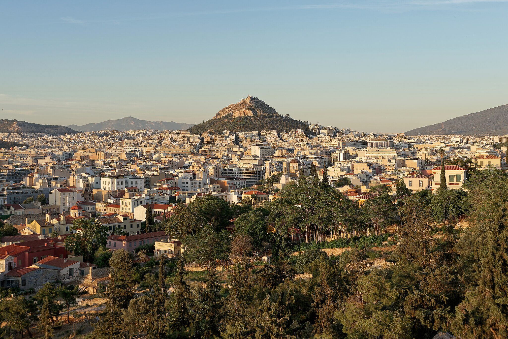 A view of Athens at sunset, the orange light is spread across the buildings with the Acropolis in the middle towering over the city,