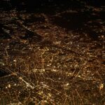 An aerial view of a city at night, showcasing a vast network of illuminated streets and buildings. The city lights form intricate patterns against the dark backdrop, highlighting the urban landscape.