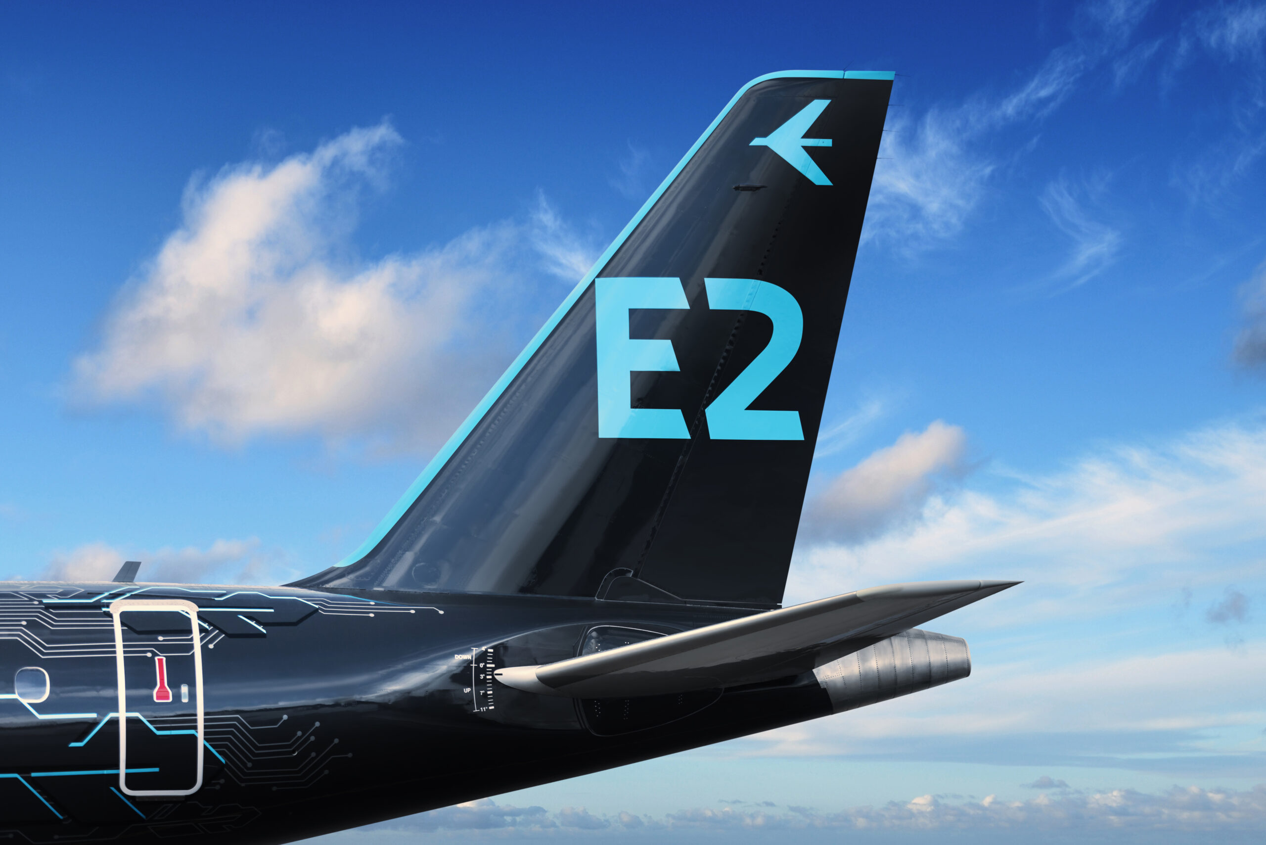 The image shows the tail section of a modern aircraft against a blue sky with scattered clouds. The vertical stabilizer is painted black with light blue accents and prominently displays the characters "E2" in large, light blue font. Above the "E2" is a stylized bird logo in the same light blue color. The fuselage near the tail features circuit-like patterns and a small red thermometer symbol within a white outline.