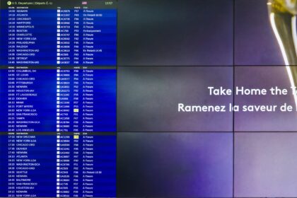 The image shows a digital departure board at an airport displaying flight information for U.S. departures. The board lists various destinations, flight numbers, gates, and statuses in both French and English. On the right side of the image, there is a partial advertisement with the text "Take Home the Taste" and "Ramenez la saveur de" in white letters on a purple background.