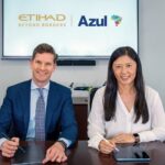 Two individuals are seated at a table, each holding a stylus and tablet. They are in front of a screen displaying the logos of Etihad Airways and Azul Brazilian Airlines.