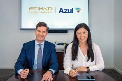 Two individuals are seated at a table, each holding a stylus and tablet. They are in front of a screen displaying the logos of Etihad Airways and Azul Brazilian Airlines.