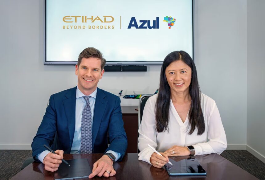 Two individuals are seated at a table, each holding a stylus and tablet. They are in front of a screen displaying the logos of Etihad Airways and Azul Brazilian Airlines.