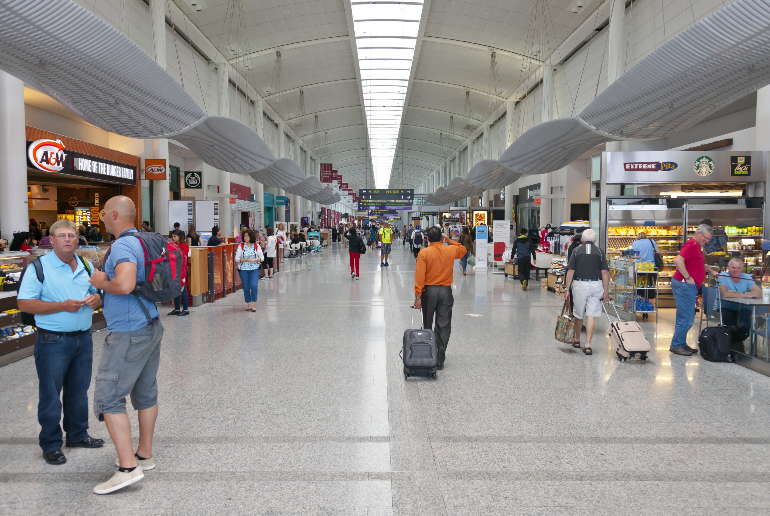 The long hallway of Toronto airport terminal 1, with shops and passengers lining either side.