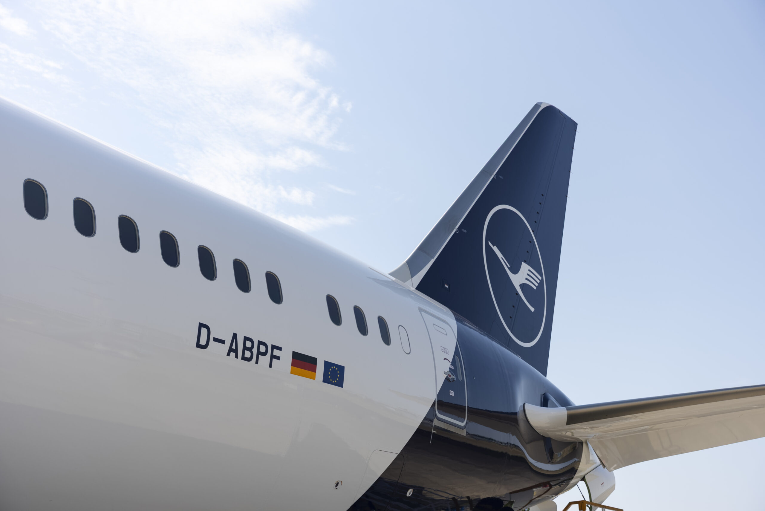 A close-up view of the rear section of a Lufthansa aircraft, showing the tail fin with the airline's logo and part of the fuselage. The registration number "D-ABPF" is visible along with German and European Union flags.