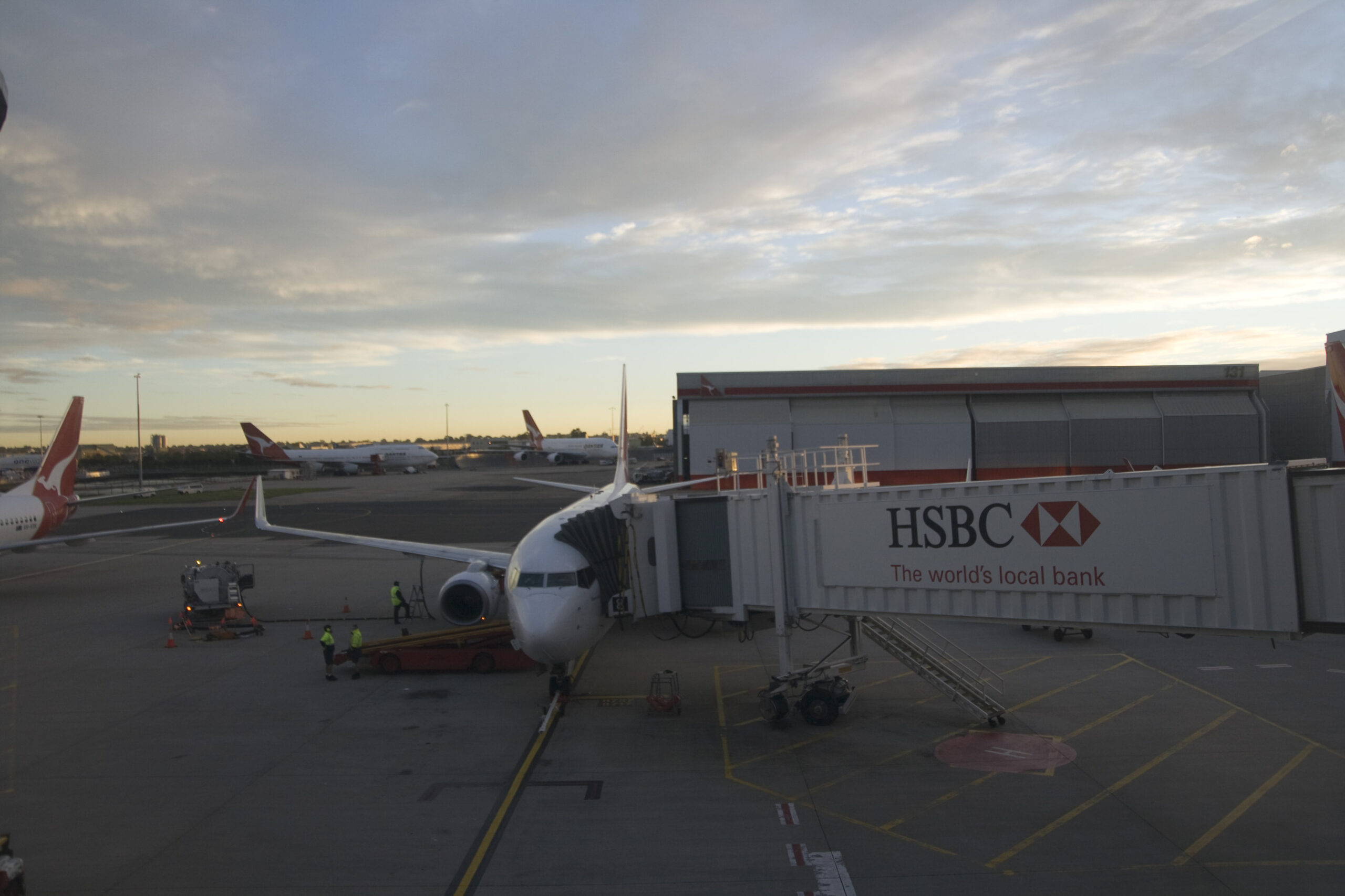 A Qantas Boeing 737 at an overcast Sydney Airport with a jetbridge.
