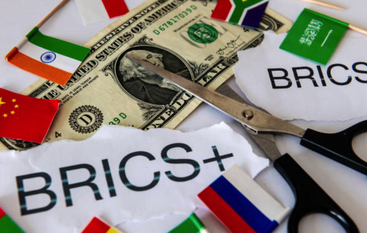 Scissors cutting a US dollar bill with BRICS and BRICS+ text surrounded by flags of China, India, Russia, South Africa, and Saudi Arabia