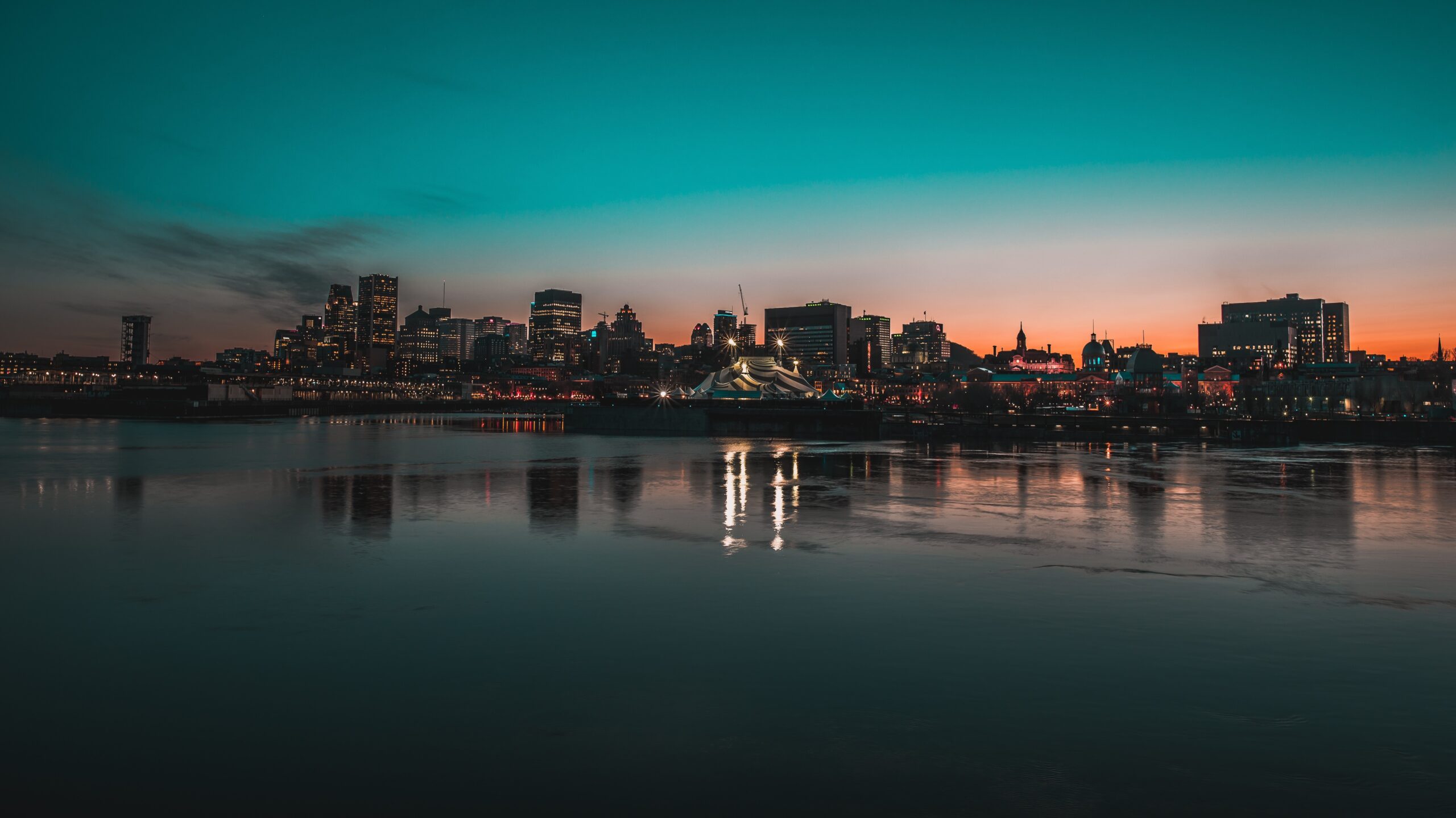 Montreal's skyline at dusk, with skyscrapers and city lights reflected i the water below.
