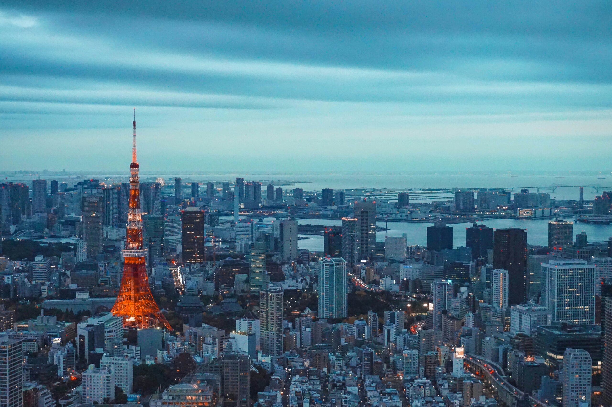 Aerial view of Tokyo cityscape at dusk with the illuminated Tokyo Tower prominently in the center, surrounded by numerous high-rise buildings and skyscrapers.