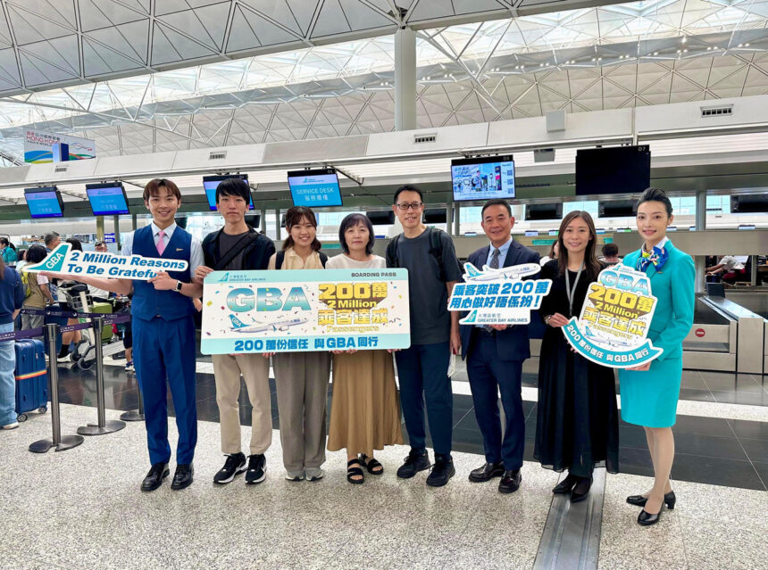 A group of people standing in an airport terminal holding signs celebrating Greater Bay Airlines' milestone of 2 million passengers. The signs read "GBA 2 Million Reasons To Be Grateful".
