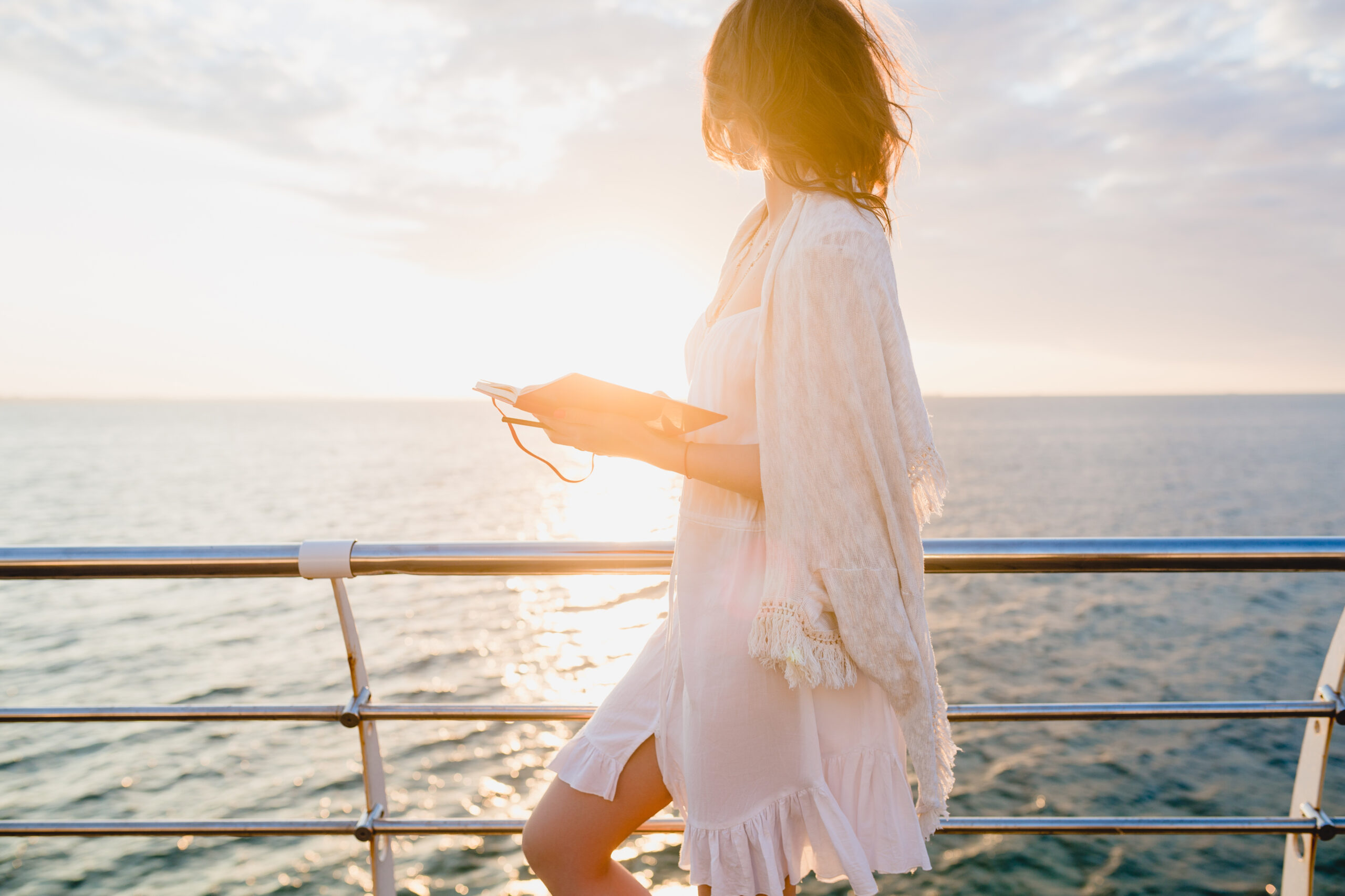 A women in a white dress on board of a cruise ship making notes in a diary