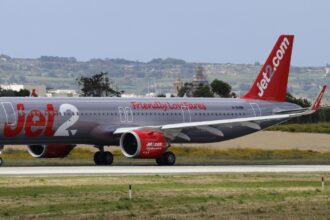 A Jet2.com plane, in silver and red colours, on the runway at an airport.