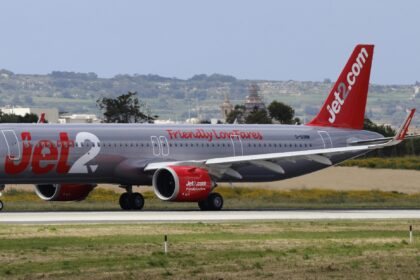 A Jet2.com plane, in silver and red colours, on the runway at an airport.