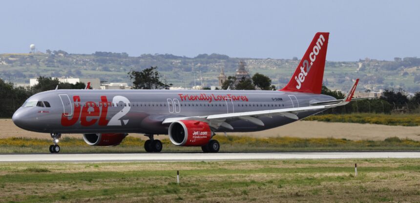 A Jet2.com plane, in silver and red colours, on the runway at an airport.