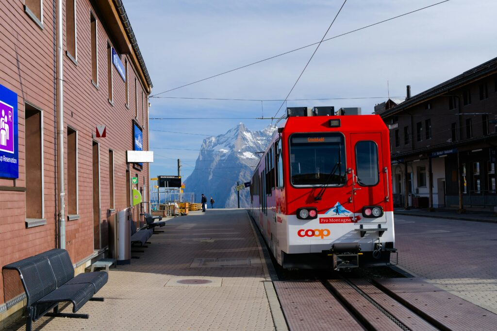 A picture of a Swiss train at a train station with a mountain in the background.