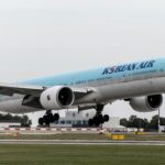 A Korean Air plane taking off from the runway with a light blue and silver body and landing gear out.