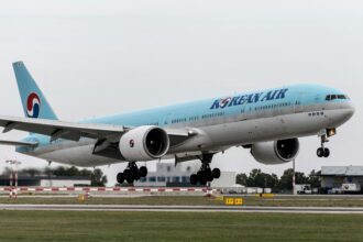 A Korean Air plane taking off from the runway with a light blue and silver body and landing gear out.