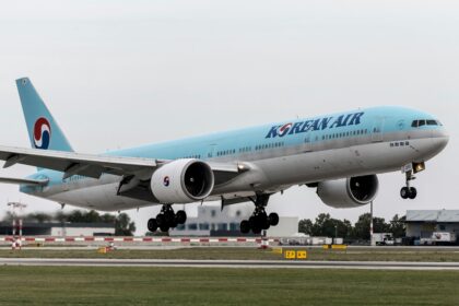 A Korean Air plane taking off from the runway with a light blue and silver body and landing gear out.
