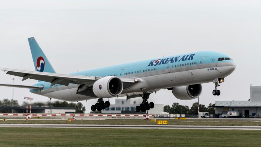 A Korean Air plane taking off from the runway with a light blue and silver body and landing gear out.