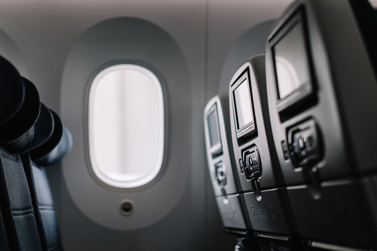 Rows of airplane seats with personal entertainment screens overlook a bright window