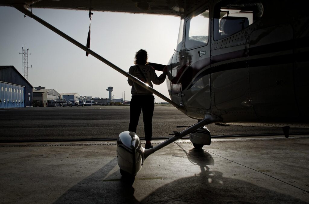 A female pilot stands beside a small aircraft at dawn, preparing for flight on a quiet airfield