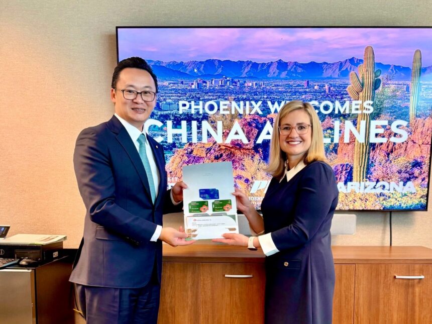 China Airlines President Kevin Chen and Phoenix Mayor Kate Gallego stand side by side holding an open folder with documents, in front of a screen that reads “PHOENIX WELCOMES CHINA AIRLINES” with a desert landscape background.