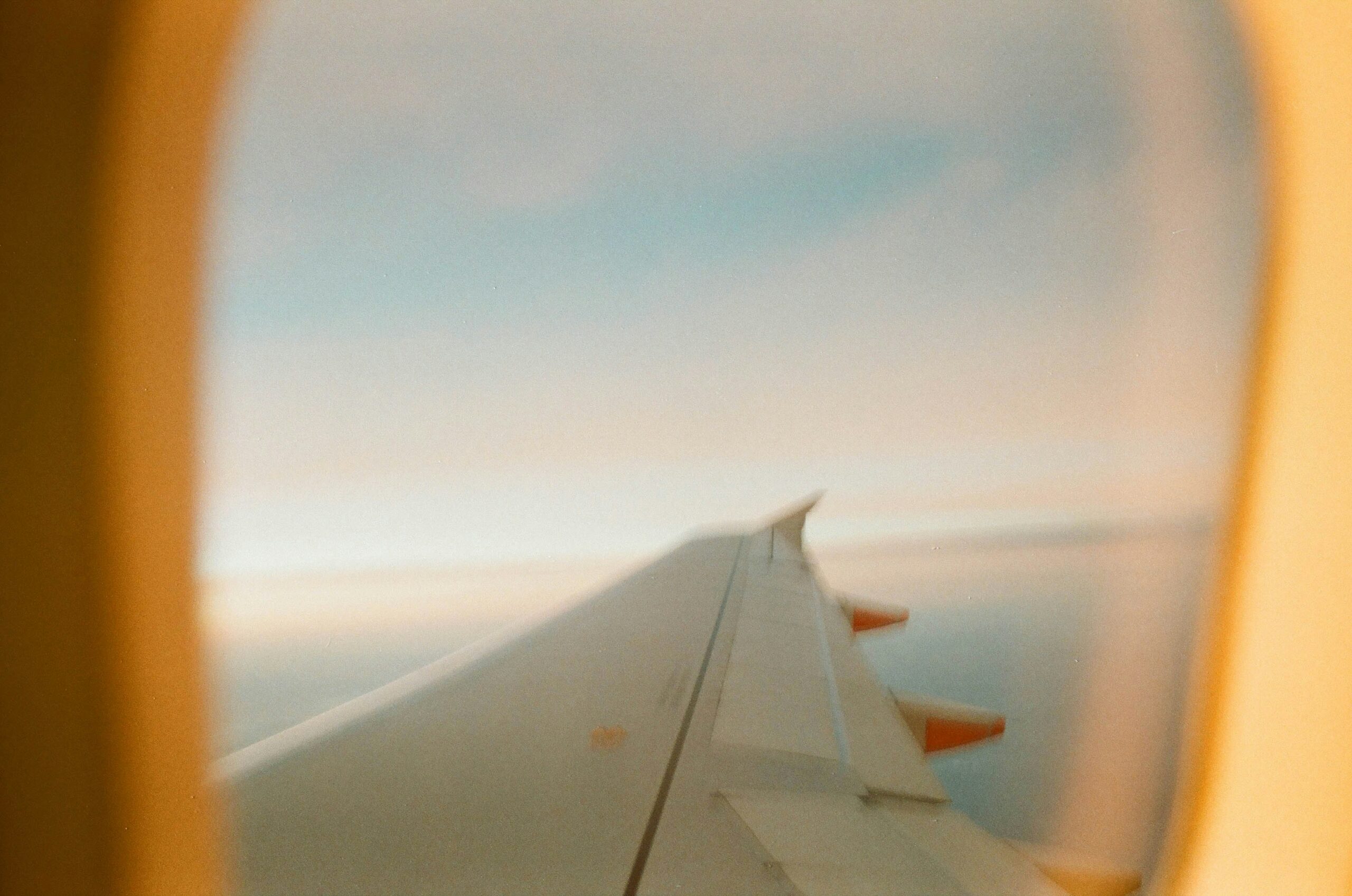 A view from an airplane window showing the wing of the aircraft against a backdrop of a clear sky with soft hues of blue and orange.