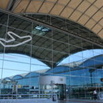 The glass front of the Alicante airport departures building, with a white outline of a plane visible on the corner.
