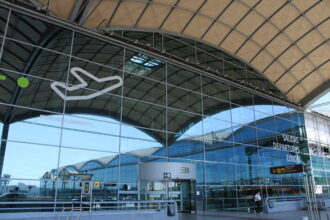 The glass front of the Alicante airport departures building, with a white outline of a plane visible on the corner.