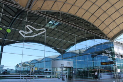 The glass front of the Alicante airport departures building, with a white outline of a plane visible on the corner.