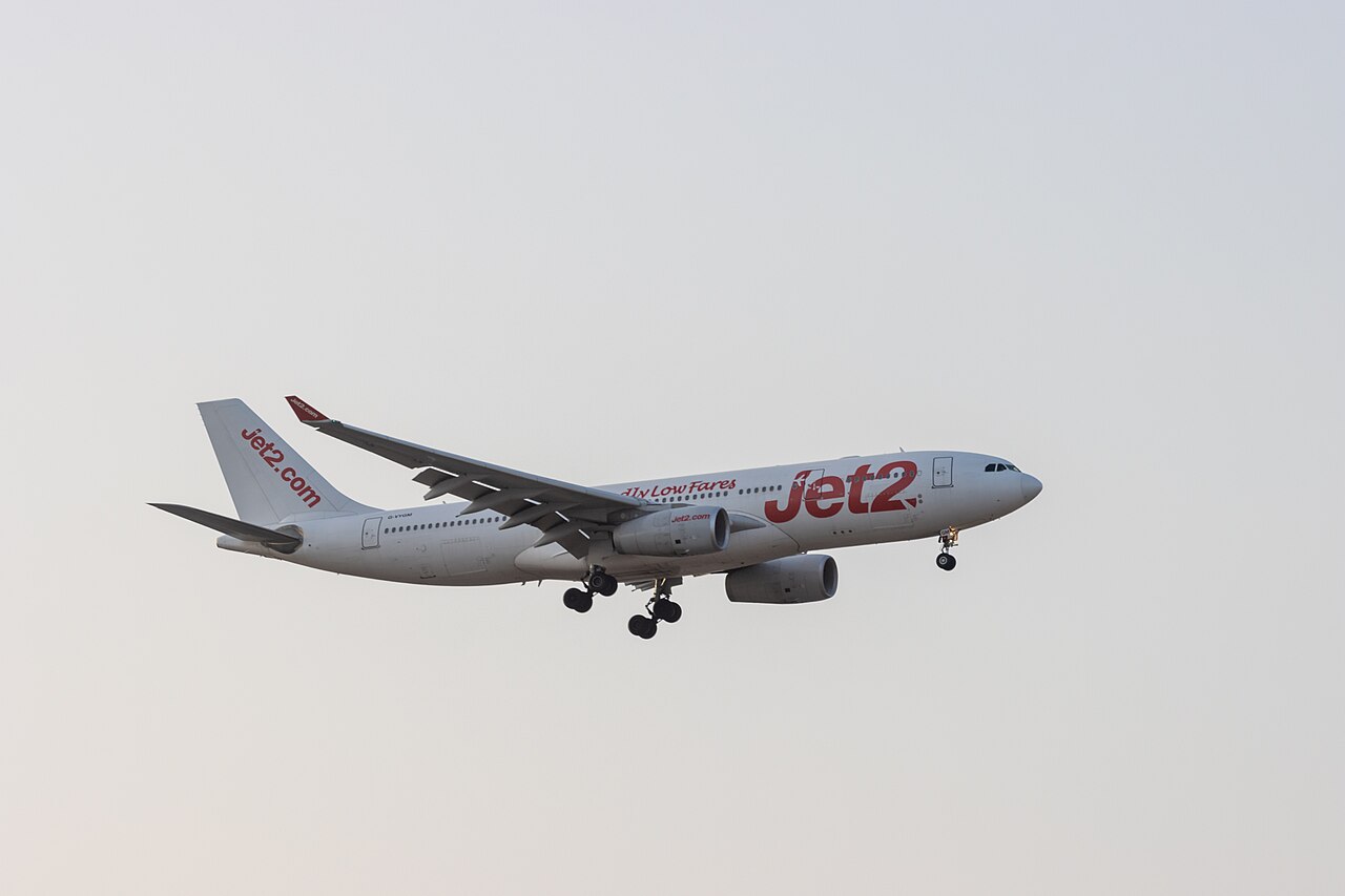 A Jet2.com airplane is captured mid-flight against a clear sky. The aircraft's landing gear is deployed, indicating it is preparing to land. The plane features the Jet2 logo and the slogan "Fly Low Fares" on its fuselage.
