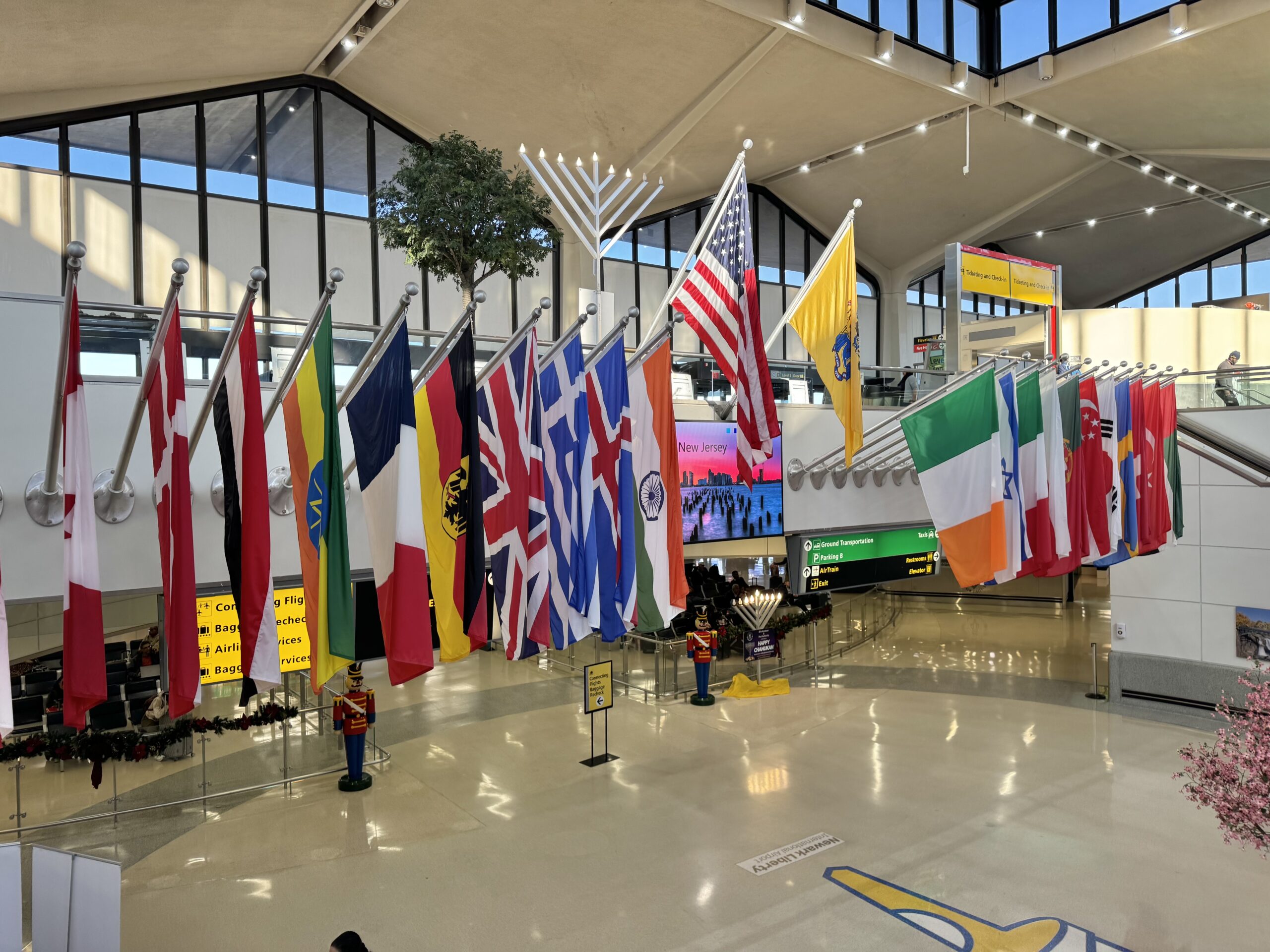 A series of flags from many countries hung in an airport lobby, with the USA flag in the centre.
