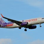 A white HK Express plane with purple and orange accents comes in for landing.