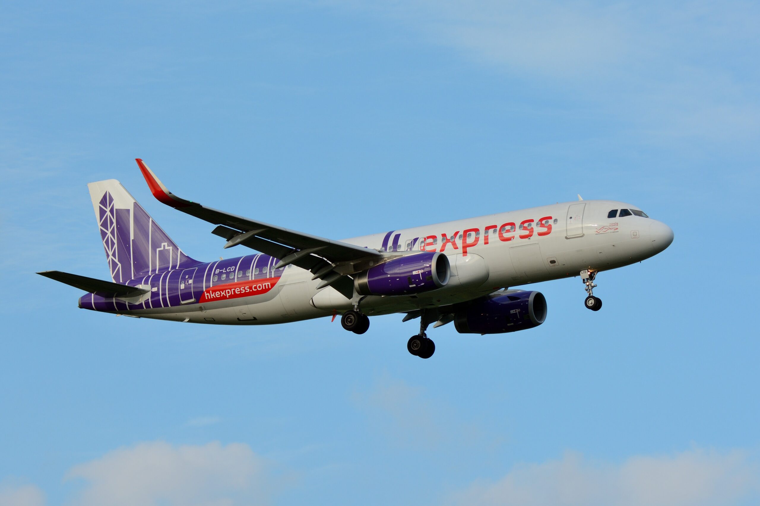 A white HK Express plane with purple and orange accents comes in for landing.