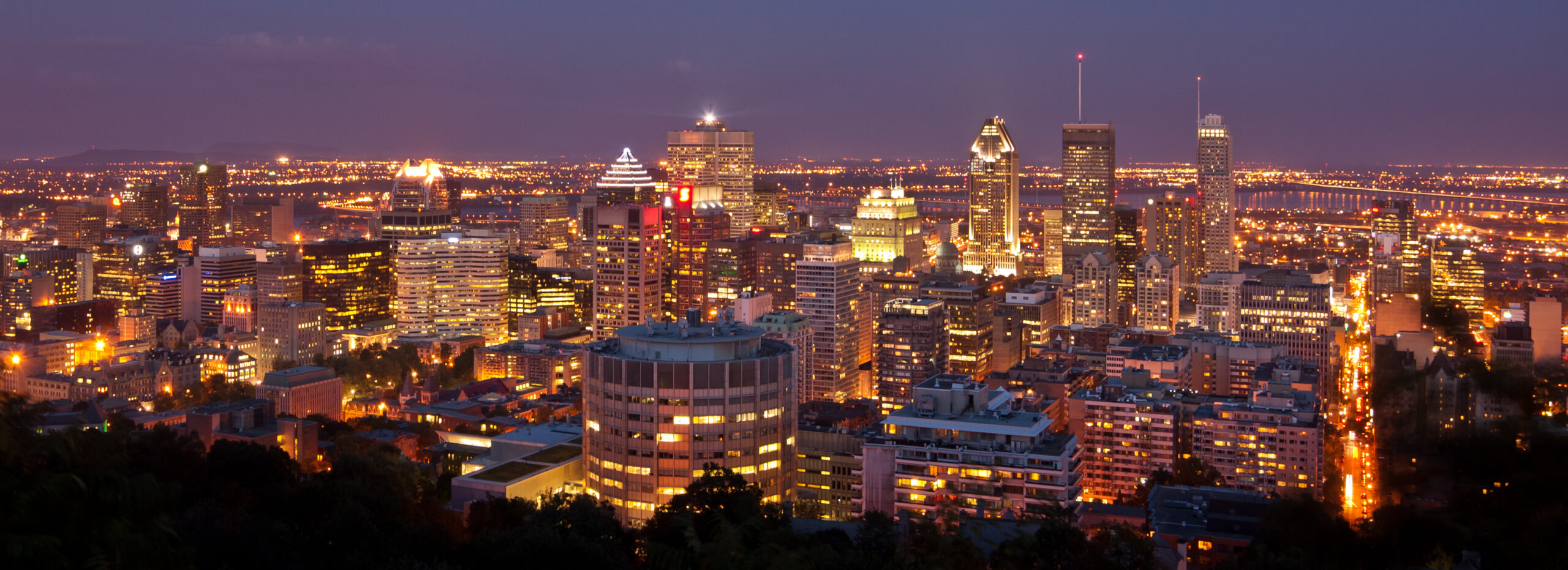 A nighttime view of Montreal from a nearby mountain, with city lights illuminating Montreal.