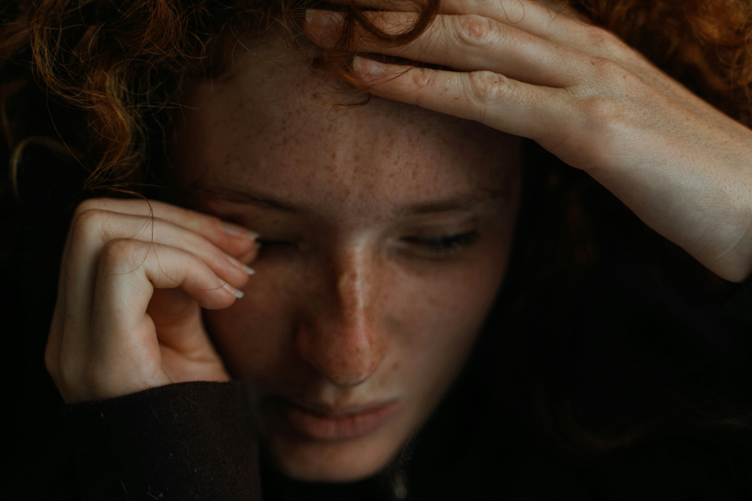 A close-up image of a person with curly hair, holding their head with both hands. The person's face is blurred, making it unrecognisable.