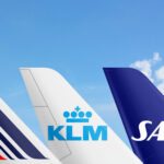 The image shows the tail sections of three airplanes from different airlines against a clear blue sky. From left to right, the tails belong to Air France, KLM Royal Dutch Airlines, and Scandinavian Airlines (SAS). The Air France tail features a design with blue and red stripes and a small circle of yellow stars. The KLM tail is white with the airline's blue logo, which includes a crown symbol. The SAS tail is dark blue with the airline's white logo.