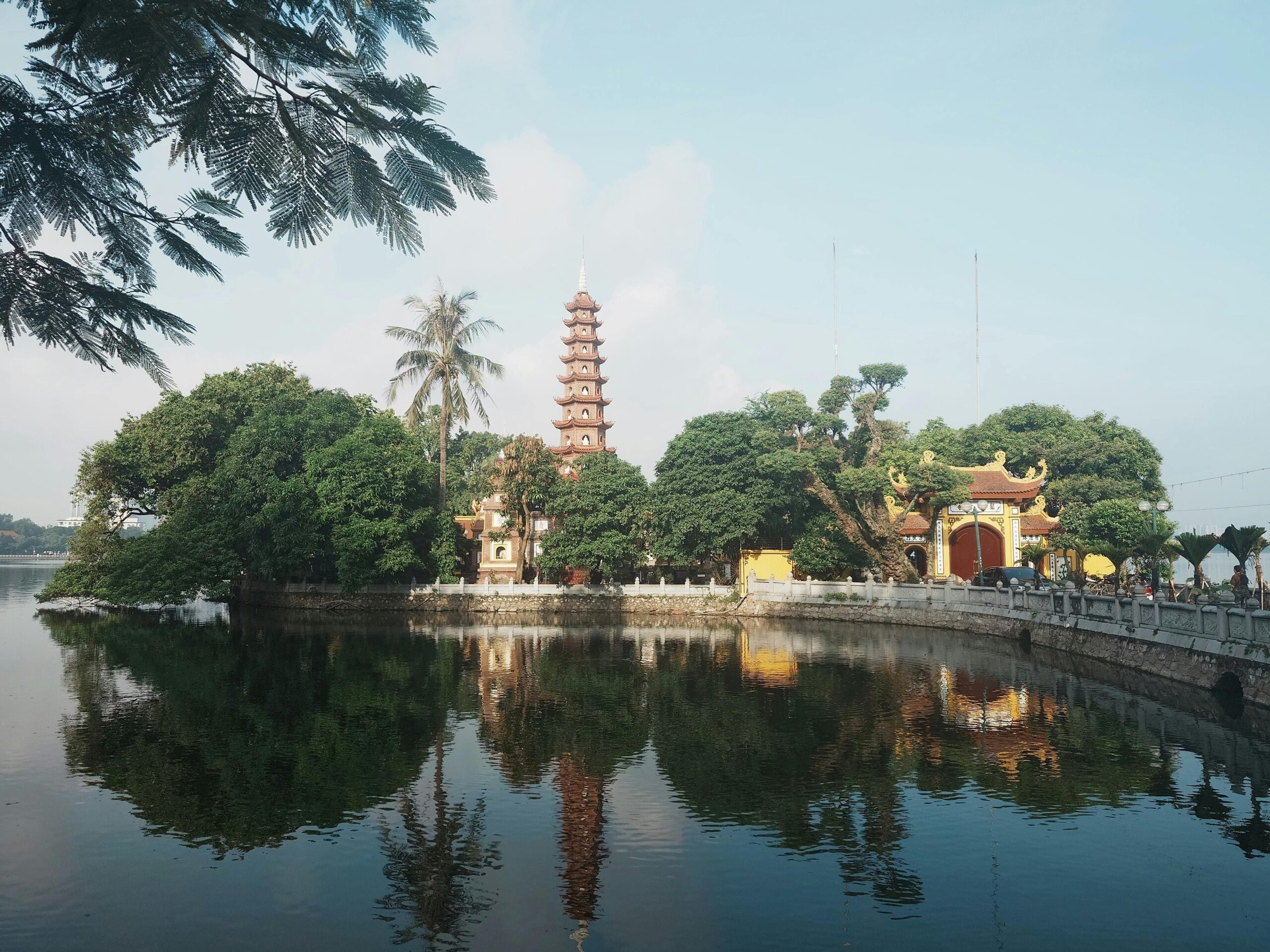 A traditional Vietnamese Pagoda reflected in the river below, surrounded by trees and foliage.