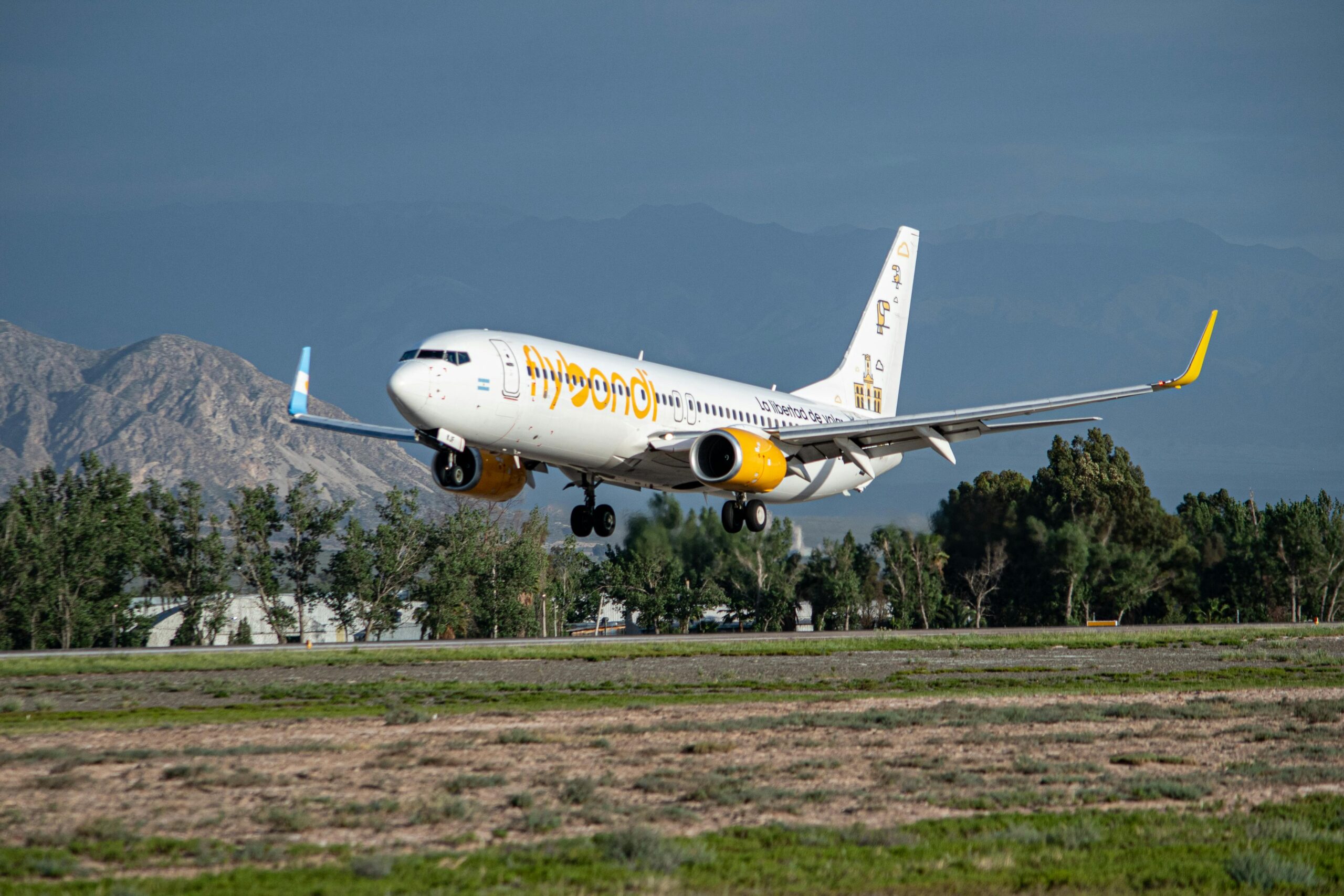 A Flybondi flight coming in for landing at a scenic airport with a mountainous background.