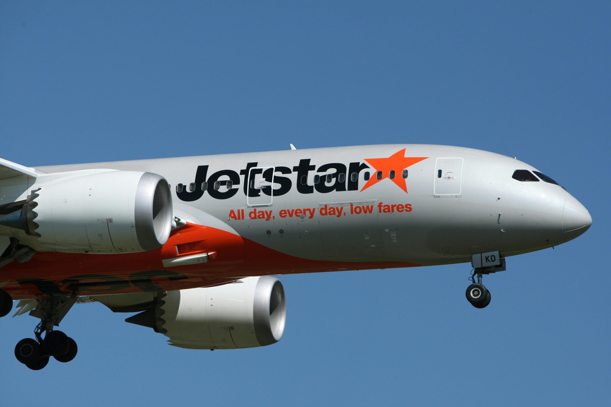 A zoomed in picture of the silver and orange front of a Jetstar aircraft as it flies through the sky.