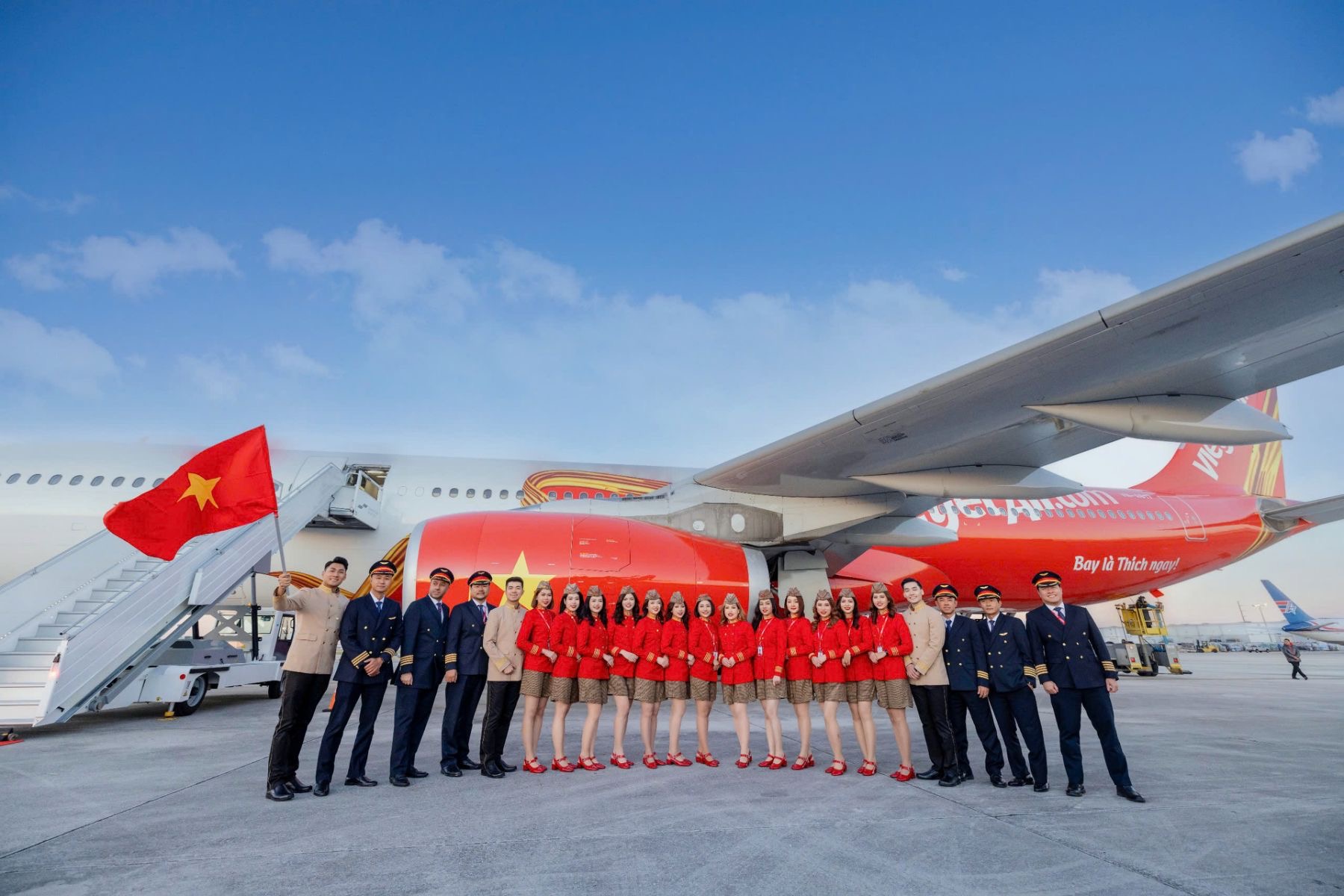 A Vietjet flight crew in front of the new Airbus A330 aircraft, which has a red and white livery with a yellow ribbon flowing across the aircraft.
