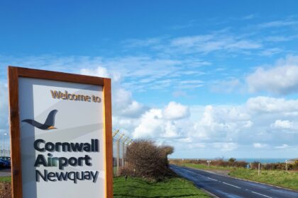 Cornwall Airport Newquay sign by the road, surrounded by grass. Blue sky with some white clouds in the background.