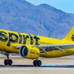 A yellow Spirit Airlines plane landing with mountains in the background.