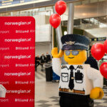 A LEGO figure next to a Billund Airport and Norwegian signboard.